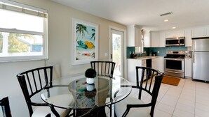 A modern kitchen with white cabinets, stainless steel appliances, and a glass dining table with black chairs. - Anna Cabana B: Pool Home, AMI North End, 2 Blocks to Beach by Anna Maria Life Vacation Rentals (Anna Maria)