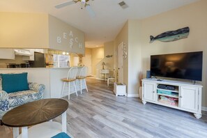 Una sala de estar con sofá, sillas, una mesa de centro, televisor y una zona de cocina.