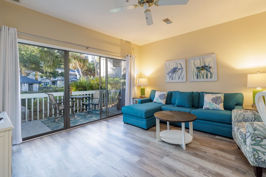 A living room with a blue sofa, a round coffee table, and a balcony with a glass door.