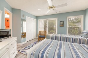 Ein Schlafzimmer mit zwei Betten, einem Deckenventilator, einer Kommode und einem Fenster mit Jalousien.