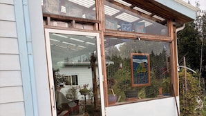 Une maison avec une grande fenêtre, une porte en bois et un tuyau d’arrosage dans le jardin.