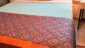 Un lit avec une couvre-lit à motifs, une tête de lit en bois et des oreillers ornés de motifs géométriques.