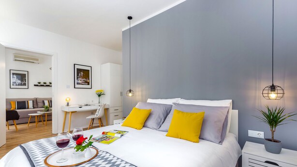 Et moderne hotelværelse med en stor seng, et natbord med lampe, et lille skrivebord og en potteplante.