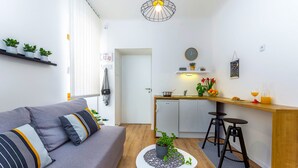 En moderne stue med en grå sofa, et lille sofabord og et køkkenområde med en træbordplade og to sorte barstole.