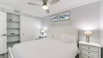 Een slaapkamer met een bed, nachtkastjes, een plafondventilator en kunst aan de muur.