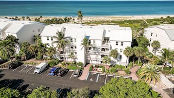 A multi-story hotel with a parking lot, surrounded by palm trees and a view of the beach.
