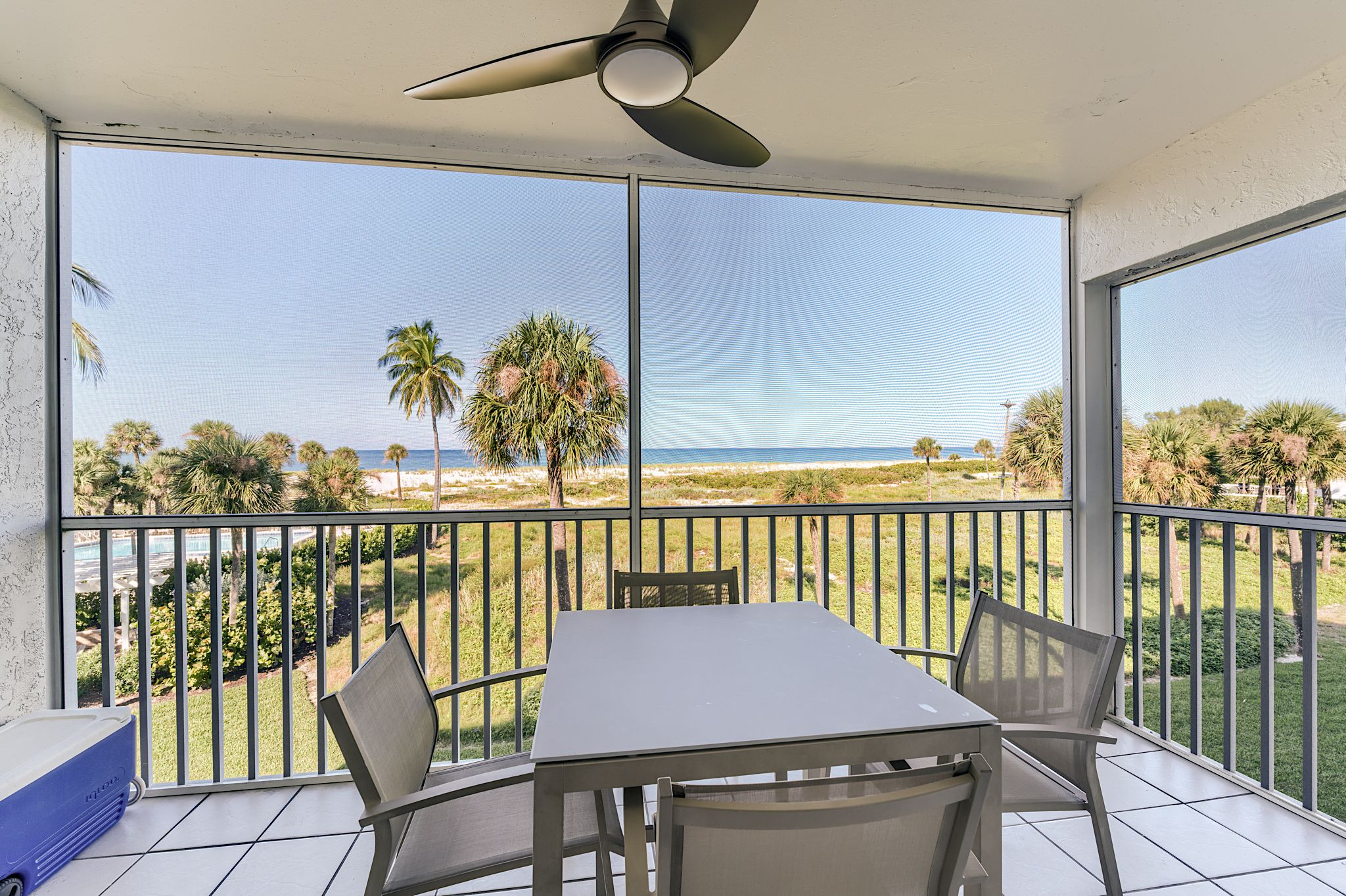 Ein Balkon mit Tisch und Stühlen mit Blick auf einen Strand und Palmen.