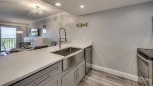 A modern kitchen with a large island, stainless steel appliances, and a view to the outdoors. - Stunning Modern beach front unit - completely renovated!  Includes golf cart! (Captiva)