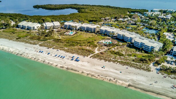 An aerial view of a coastal resort with multiple hotel buildings, a sandy beach, and a clear view of the ocean. - Stunning Modern beach front unit - completely renovated!  Includes golf cart! (Captiva)