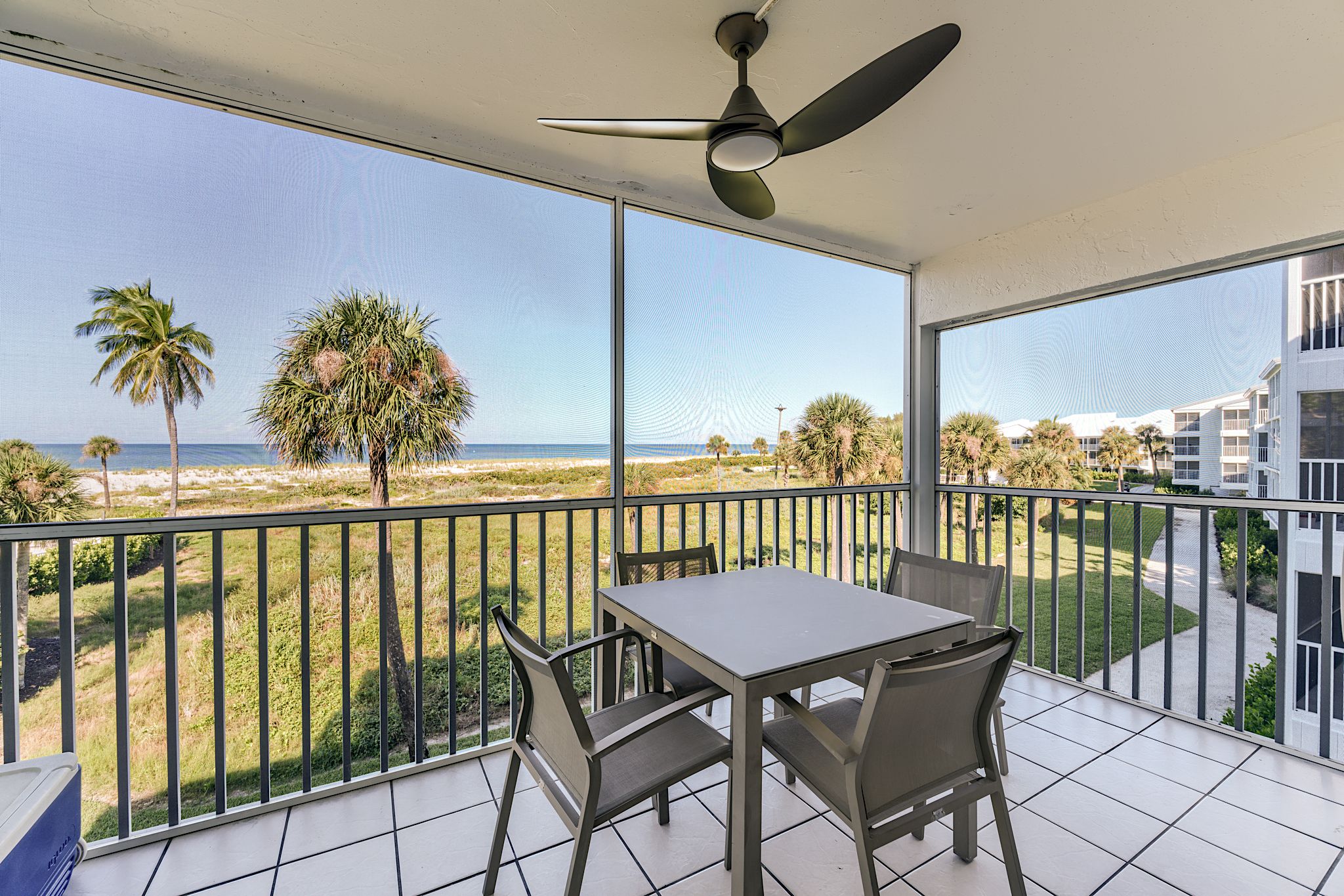 A balcony with a table and chairs, overlooking a beach and palm trees.