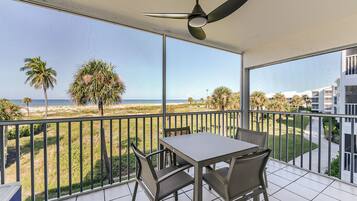 A balcony with a table and chairs, overlooking a beach and palm trees.