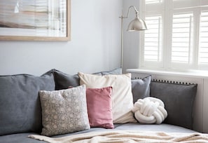 A grey sofa with multiple cushions, a floor lamp, and a window with blinds.
