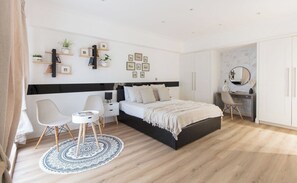 A modern bedroom with a bed, bedside table, chair, and a desk with a chair. There are wall-mounted shelves with decorative items.
