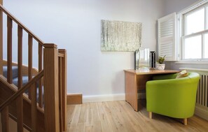A room with a wooden staircase, a desk with a plant, a green chair, and a radiator.
