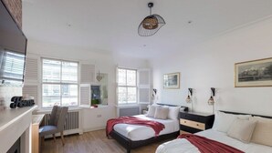 A bedroom with two beds, a radiator, a chair, and a window with shutters. - Spacious quiet 4BR/6beds house with private garage (London)