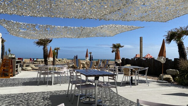 Un área de estar al aire libre con mesas y sillas, sombrillas y vistas a la playa.