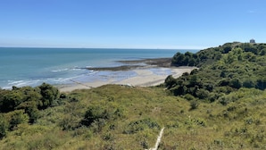 Paisaje costero con una playa, un camino y una colina con una estructura en la cima.