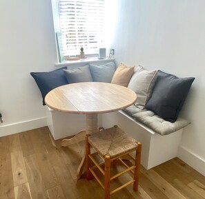 Un coin salon confortable avec une table ronde en bois, un banc rembourré et un canapé agrémenté de plusieurs coussins.