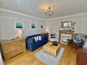 Un salon avec un canapé bleu, une commode en bois et une cheminée surmontée d’un miroir.