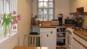 Una cocina compacta con ventana, un refrigerador pequeño, un tostador, un microondas y una mesa de madera con sillas.
