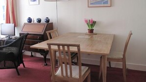 Un comedor con una mesa de madera, dos sillas, una lámpara, una planta en maceta y un cuadro en la pared.