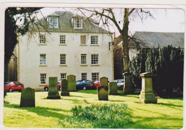 A building with multiple windows and a grassy area with headstones.