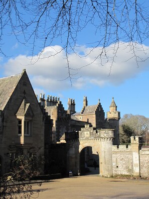 A historic stone building with a prominent archway entrance, multiple chimneys, and a tower.