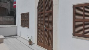 Un bâtiment à l’extérieur blanc, doté d’une grande porte en bois et de volets persiennés, ainsi que d’une fenêtre plus petite également pourvue de volets.