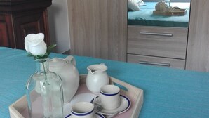 Un plateau de petit-déjeuner soigneusement préparé, avec une théière, est posé sur un lit recouvert d’une couverture bleue.