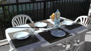 Une table blanche installée à l’extérieur, avec des assiettes, des verres et une bouteille d’eau, entourée de chaises blanches.