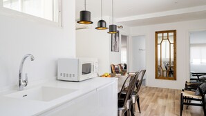 Una cocina moderna con encimera blanca, microondas integrado y fregadero. Tres lámparas colgantes iluminan la encimera.