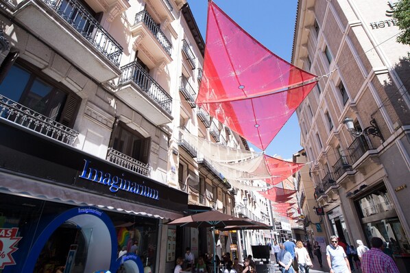 Una calle con edificios, incluyendo un hotel con balcones y una tienda llamada 'Imaginaryum'.