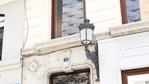 Un edificio con una puerta doble marrón oscuro, una farola y un ventanal con reflejos.