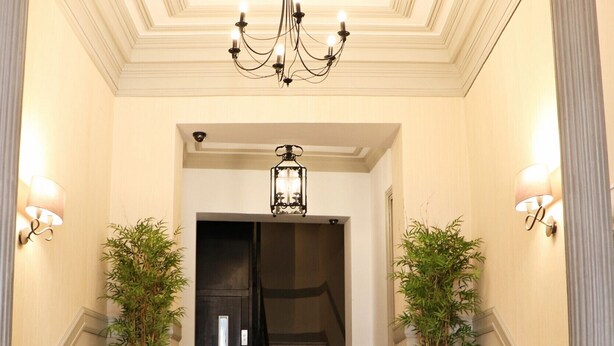 Una majestuosa escalera de mármol, flanqueada por dos grandes macetas con plantas y un candelabro colgante.