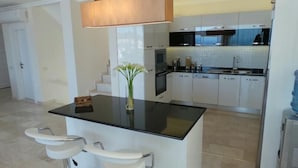 Une cuisine moderne avec des meubles blancs, un plan de travail noir et un petit îlot central doté de tabourets de bar.