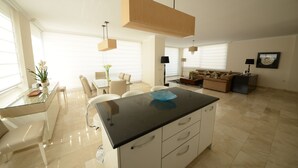 Une cuisine moderne dotée d’un îlot central en verre, de meubles blancs et de luminaires suspendus.