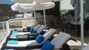 Une rangée de chaises longues avec des serviettes bleues, des parasols blancs et une vue sur une colline.