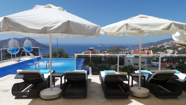 Un espace aménagé au bord de la piscine, avec des chaises longues et des parasols, offrant une vue sur la piscine et un panorama magnifique sur la mer et les collines.