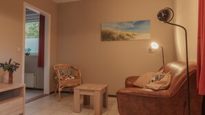 Un salón con un sofá de cuero marrón, una silla de mimbre, una mesita de madera, una lámpara de pie y un cuadro de un faro en la pared.