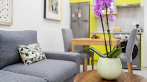 A living room with a grey sofa, a patterned pillow, and a vase with purple orchids on a wooden table.