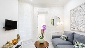 A modern living room with a grey sofa, a round coffee table, and a flat-screen TV mounted on the wall.