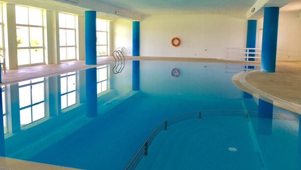 Una piscina interior con agua azul cristalina, rodeada de pilares azules y paredes blancas.