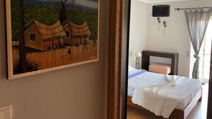 Un dormitorio con una cama, una mesita de noche, una lámpara y un cuadro de un paisaje de pueblo en la pared.