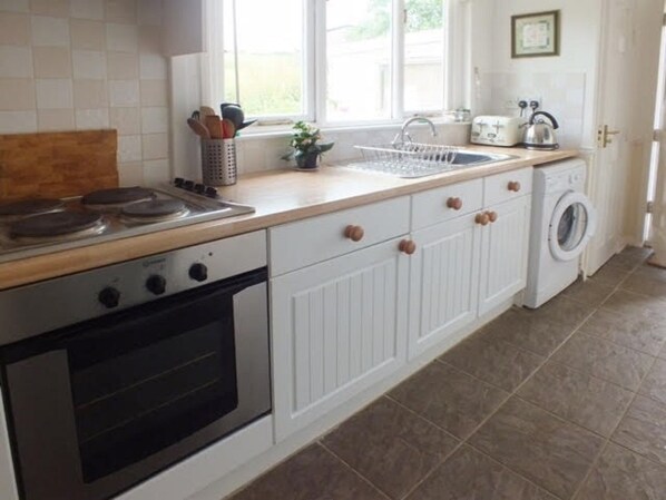A kitchen with white cabinets, a stove, a sink, and a washing machine. - The Bailiff's House - Perfect for multiple dogs and their family.  (Cornwall)