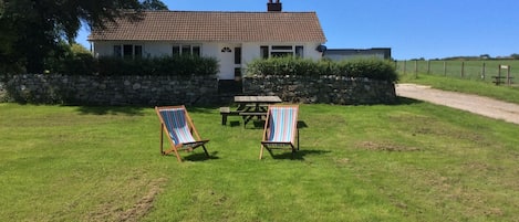 A house with a stone wall, a grassy lawn, and two beach chairs.