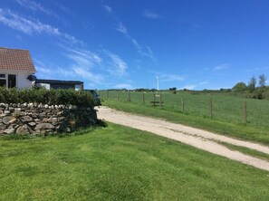 A rural road leading to a house with a stone wall and a wind turbine in the background.