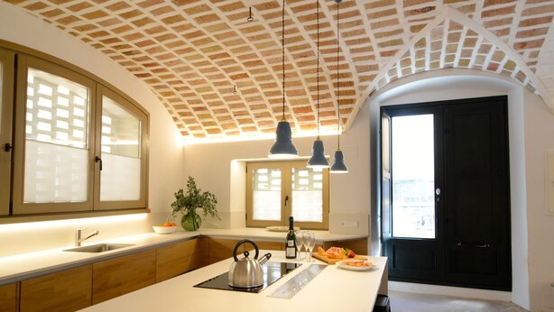 A modern kitchen with a large island, pendant lighting, and a view of the city through the window. - CASA ROSA DEL PORT (L'Escala)