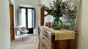 A hallway with a white chair, a wooden dresser with a vase of flowers, and a framed poster on the wall. - CASA ROSA DEL PORT (L'Escala)