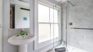 Een badkamer met een wit wastafelmeubel, een glazen douchecabine en een raam.
