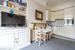 A modern kitchen with white cabinetry, a flat-screen TV, a dining table with chairs, and a decorative mirror.